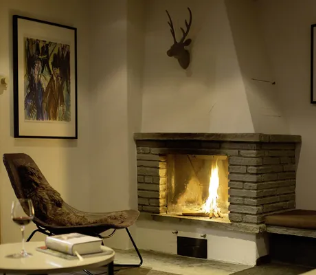 gemütlicher Sessel mit Fell vor dem Kaminfeuer im Chalet vue au lac mit Deko-Hirschgeweih und Kunstbildern an der Wand