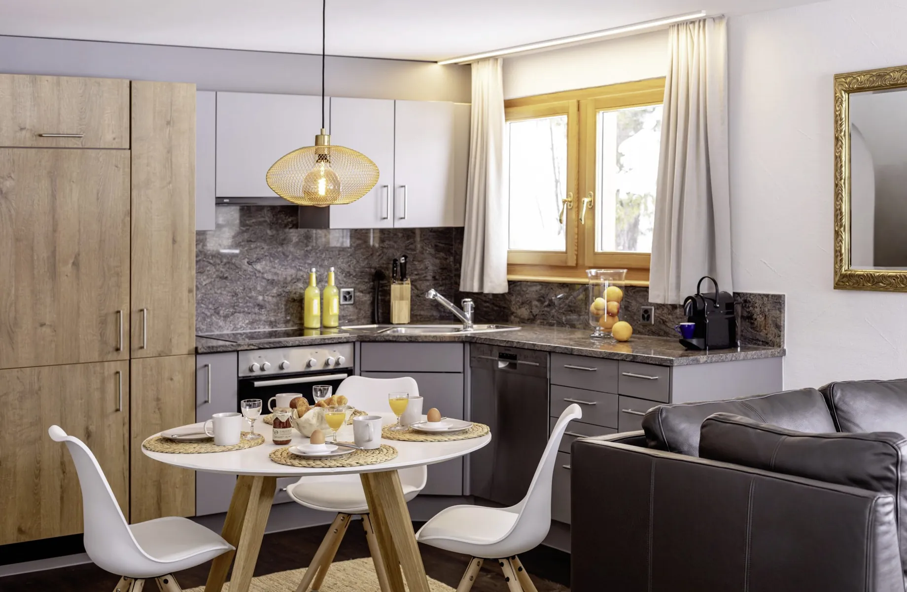 gedeckter Frühstückstisch im Chalet vue au lac mit drei weißen Stühlen, graue Küche und Holzschrank im Hintergrund