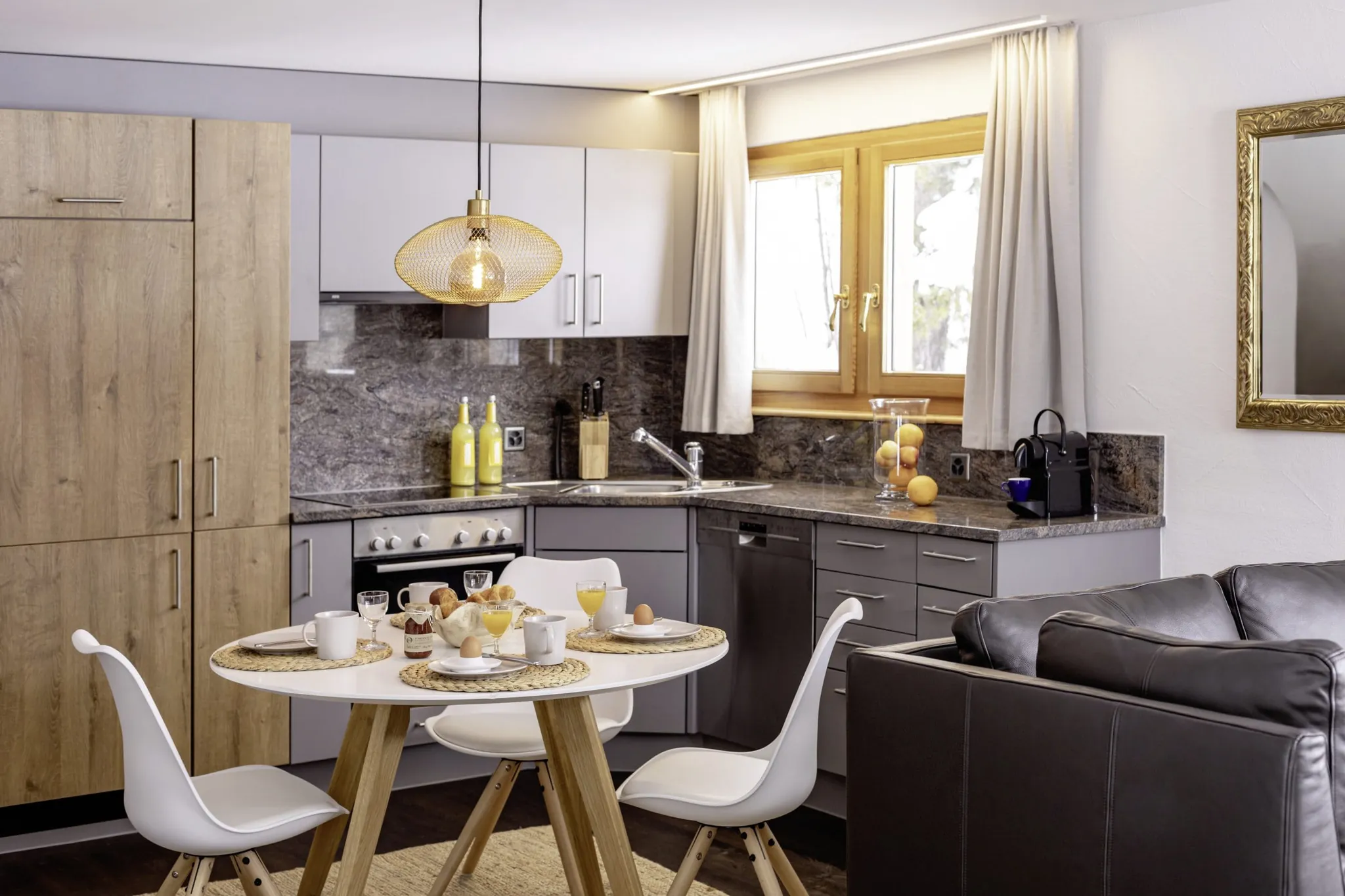 gedeckter Frühstückstisch im Chalet vue au lac mit drei weißen Stühlen, graue Küche und Holzschrank im Hintergrund
