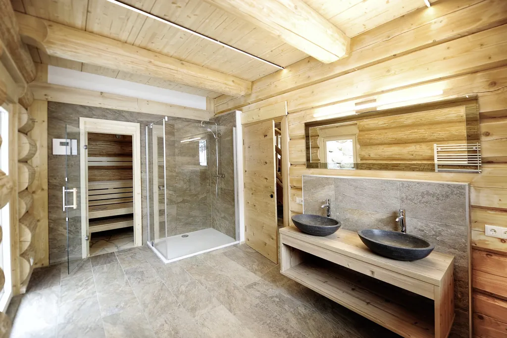 Badezimmer der Summit Lodges mit Holzwänden, zwei dunkelgrauen Stein-Waschbecken, Steinfließen-Boden, Regendusche und Sauna