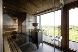 Blick in die Sky Sauna des Wellnesshotel Wittelsbach mit Holzwänden, Glasfront und Ausblick auf grüne Baumlandschaft im Hintergrund