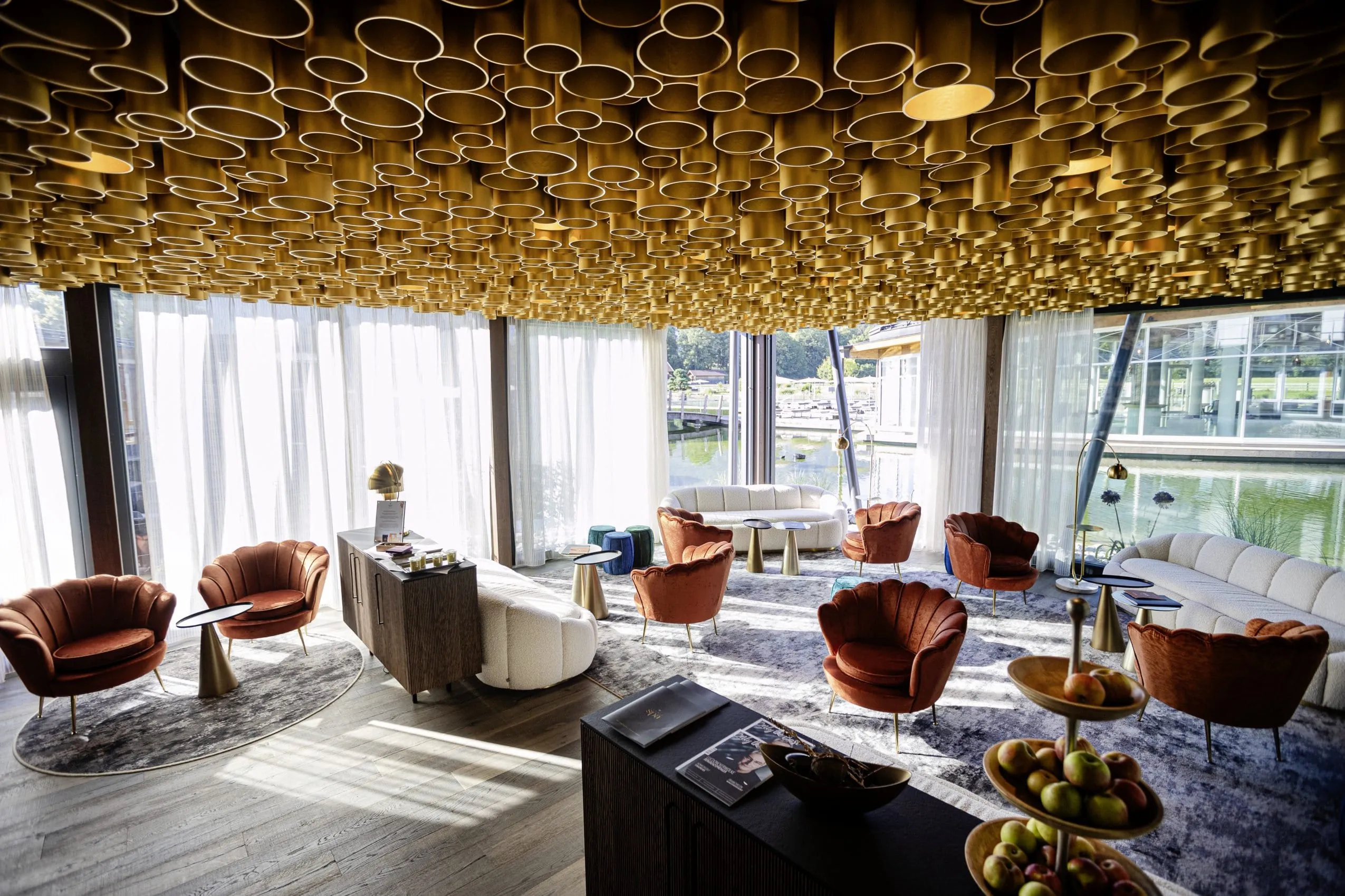 Spa-Lounge im Wellnesshotel K&ouml;nig Ludwig mit Blick auf den See, goldener Deckeninstallation und Polstersesseln in Muschelform