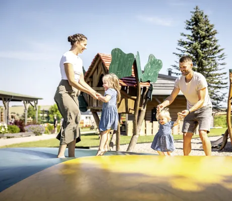 Eltern mit zwei kleinen Mädchen springen auf einem Hüpfkissen im Outdoorbereich des Familotel Elldus Resort