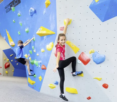 Mädchen mit rotem Sportshirt und Junge in blauem Shirt klettern an der Boulderwand des Feldberger Hof