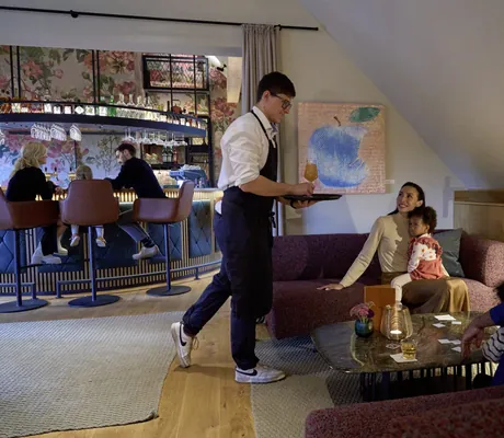Familie sitzt auf gemütlichen Sofas in der Bar des Familotel Landhaus Averbeck und Kellner kommt mit einem Drink