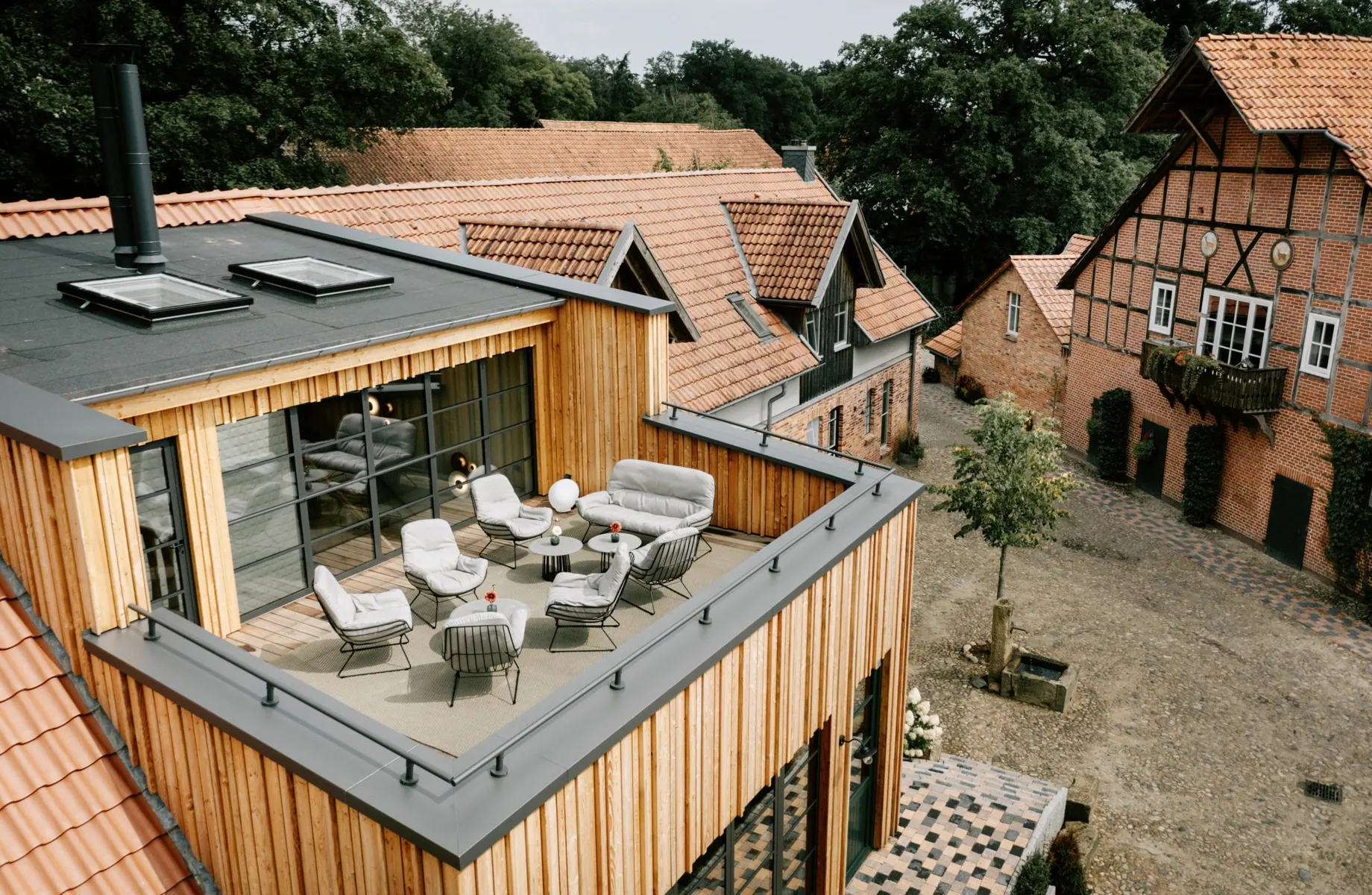 Blick auf die Dachterrasse des Familotel Landhaus Averbeck mit grauen Sitzmöbeln, Klinkersteinhäuser und Bäume im Hintergrund