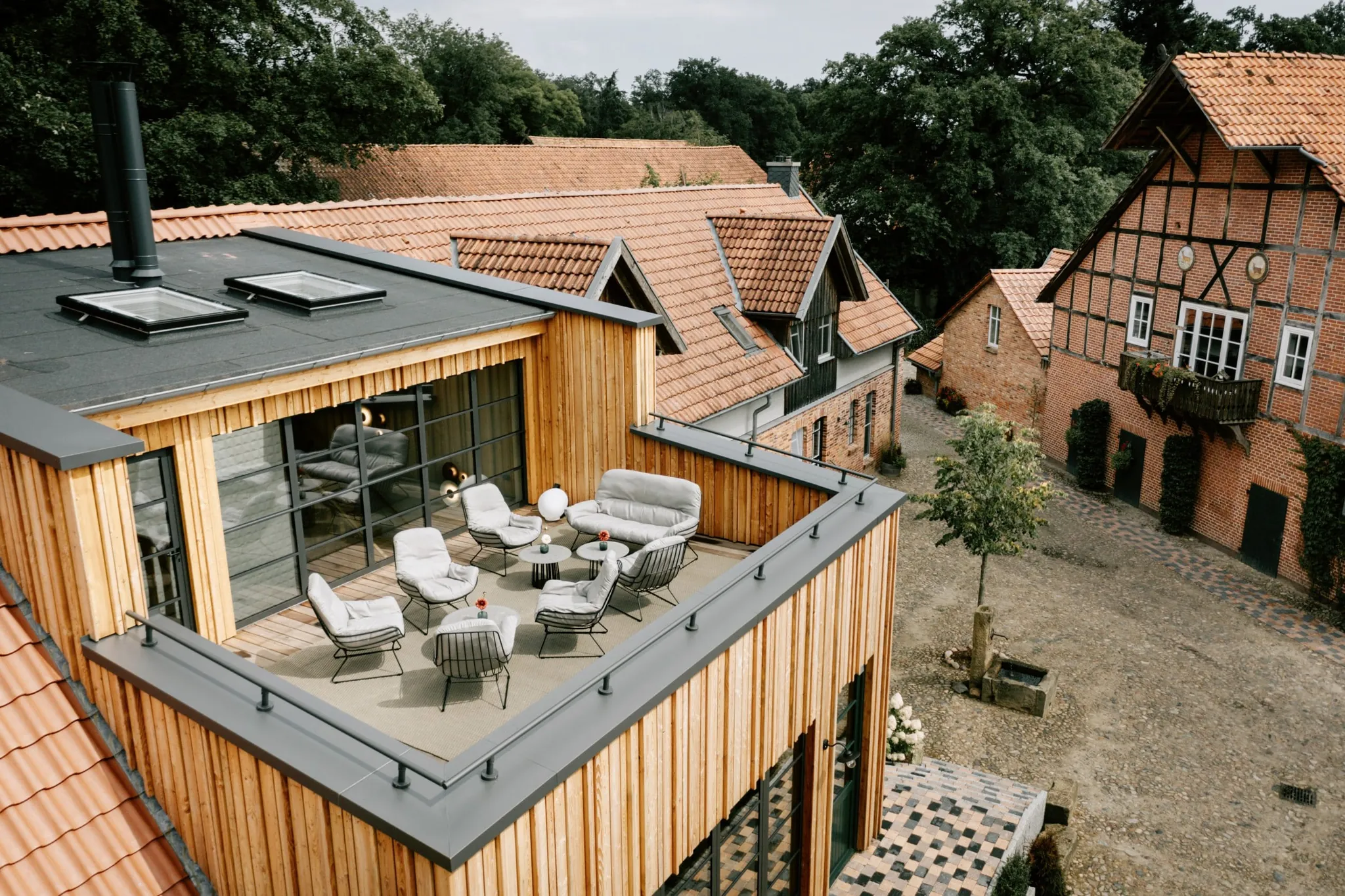 Blick auf die Dachterrasse des Familotel Landhaus Averbeck mit grauen Sitzmöbeln, Klinkersteinhäuser und Bäume im Hintergrund
