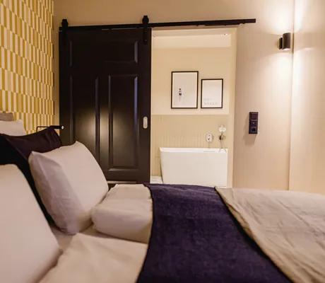 Zimmer des Familotel Landhaus Averbeck mit Doppelbett, gelb gestreifter Tapete und Badewanne im Hintergrund