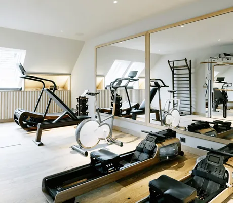 Fitnessraum des Familotel Landhaus Averbeck mit mehreren Geräten, zwei großen Spiegeln und Holzboden
