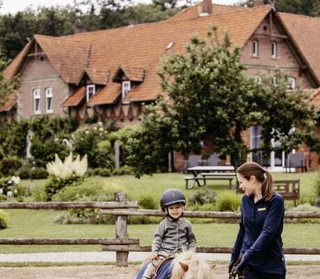 Reitlehrerin führt Junge auf einem Pony auf dem Außenreitplatz des Familotel Landhaus Averbeck