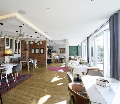 Blick in das Restaurant des Familotel Landhaus Averbeck mit unterschiedlichen Stühlen, Holztischen und Wand aus Ziegelsteinen