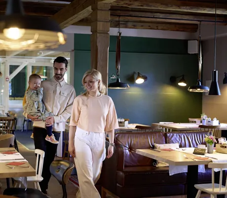 blonde Frau und Mann mit Kind auf dem Arm laufen zu ihrem Tisch im Restaurant des Familotel Landhaus Averbeck