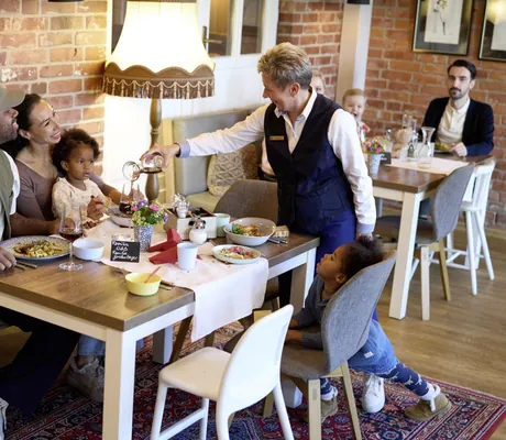 Familie sitzt im Restaurant und Kellnerin schenkt Rotwein nach im Familotel Landhaus Averbeck