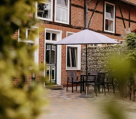 Terrasse mit Stühlen und grauem Sonnenschirm im Familotel Landhaus Averbeck mit Klinkersteinhaus im Hintergrund