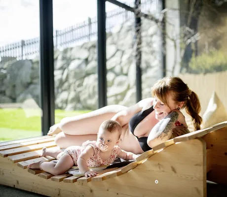 rothaarige Frau mit Zopf liegt im Spa des Landhaus Zur Ohe mit Baby auf der Holzliege
