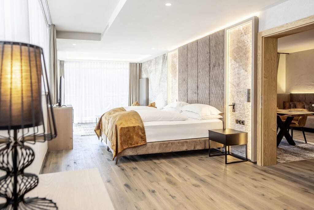Suite im Quellenhof Luxury Resort Passeier mit goldenem Bettüberwurd und Blick in den Wohnbereich