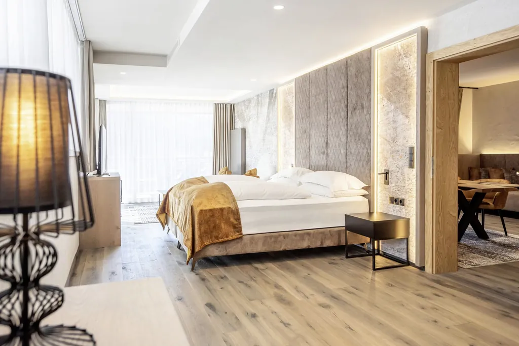 Suite im Quellenhof Luxury Resort Passeier mit goldenem Bettüberwurd und Blick in den Wohnbereich