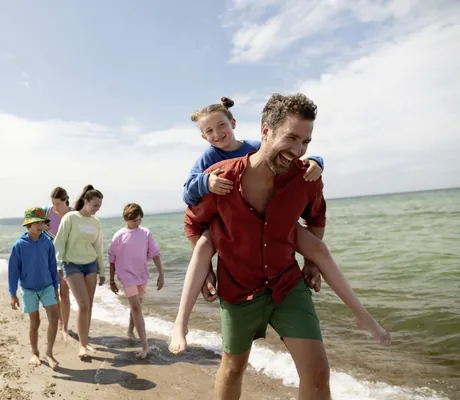 Mann in rotem Hemd trägt Mädchen Huckepack am Strand des Weissenhäuser Strand