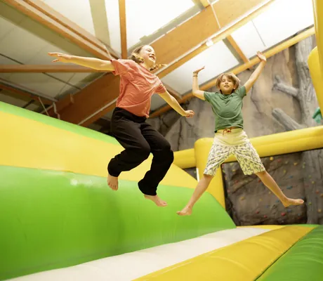 ein Junge und ein Mädchen im Teenager-Alter hüpfen auf der gelb-grünen Hüpfburg im Weissenhäuser Strand