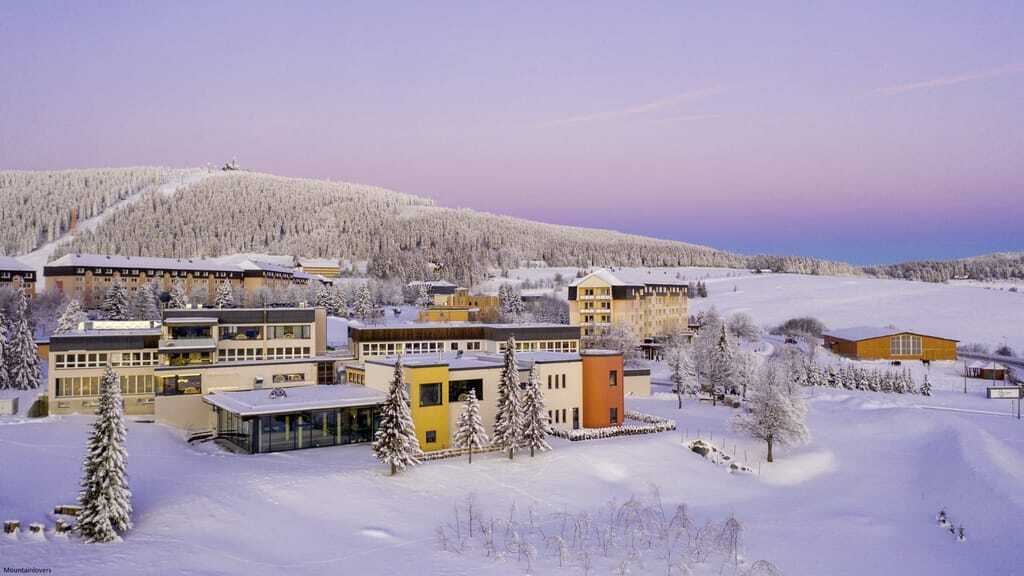 Luftaufnahme der verschiedenen Gebäude des Familotel Elldus Resort im Winter mit schneebedeckten Feldern und Bäumen
