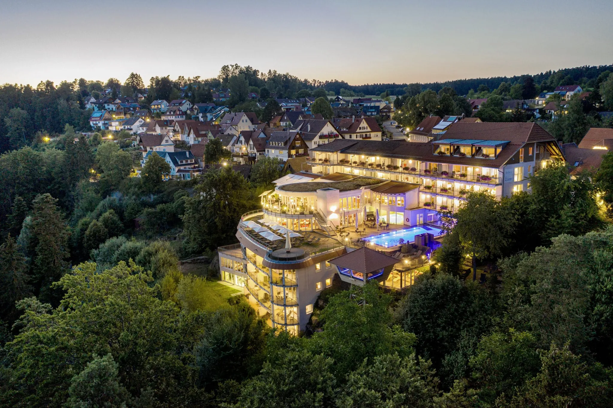 Blick aus der Luft auf das beleuchtete Hotel Kronelamm in der Dämmerung umgeben von der Natur des Schwarzwald