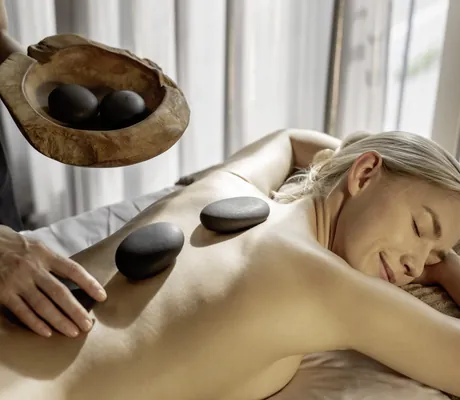 Therapeutin im Hotel 47° legt heiße Steine auf Rücken einer blonden Frau