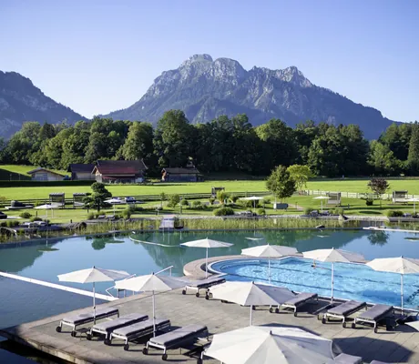 Blick auf Sportpool im Schwanensee im Das König Ludwig Inspiration SPA mit Bergen als Hintergrund