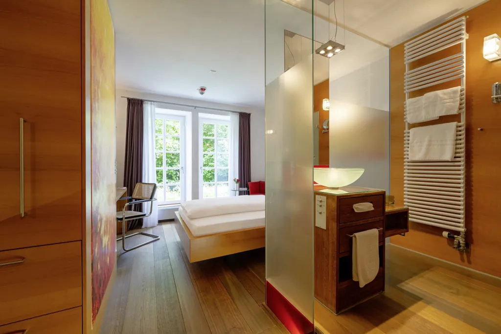 Zimmer im Schloss Lautrach mit Holzboden und Blick in das Bad mit rundem Waschbecken