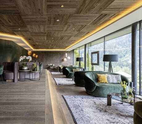Lobby des Hotel Alpenschlössel mit dunkelgrünen Sofas am Panoramafenster und beleuchteter Holzdecke