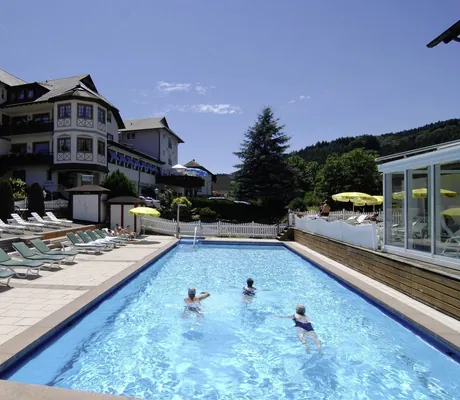 drei schwimmende Personen im Outdoorpool des Wellnesshotels Badischer Hof mit einigen Sonnenliegen und gelben Sonnenschirmen