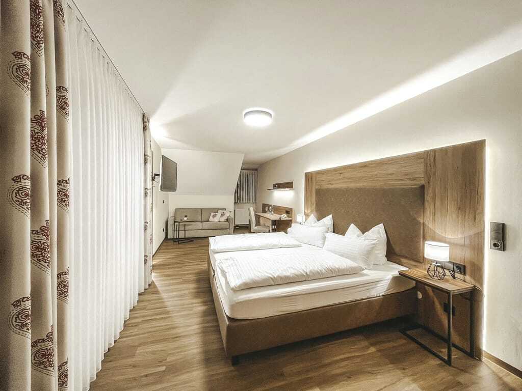 schlicht eingerichtetes Zimmer im Wellnesshotel Badischer Hof mit Holzboden, Doppelbett mit weißer Bettwäsche, TV und kleinem Sofa