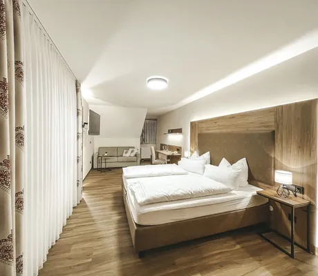 schlicht eingerichtetes Zimmer im Wellnesshotel Badischer Hof mit Holzboden, Doppelbett mit weißer Bettwäsche, TV und kleinem Sofa