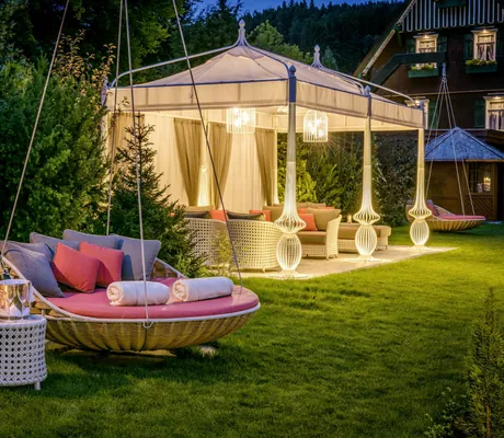 Liegewiese des Hotel Bareiss mit gemütlichen Hängeschaukeln und illuminiertem Pavillon mit Loungebereich