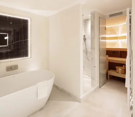 freistehende Badewanne, Dusche in Marmoroptik und Blick in die Sauna in einer Suite des Hotel Bareiss