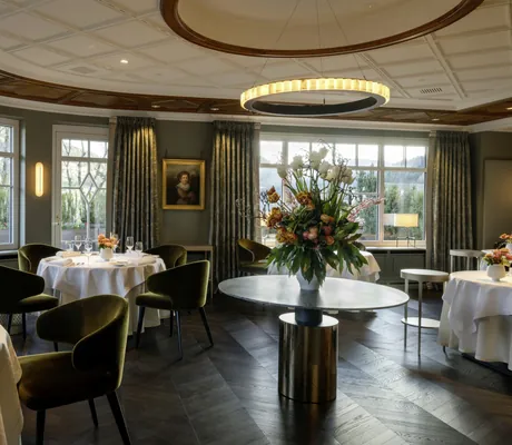 modernes Restaurant des Hotel Bareiss mit runden, mit weißen Tischdecken überzogenen Tischen, khakifarbenen Samtstühlen und großem Blumenstrauß in der Mitte