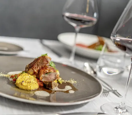 Fleischgericht im Bergland Sölden auf grauem Steingutteller neben Rotweinglas