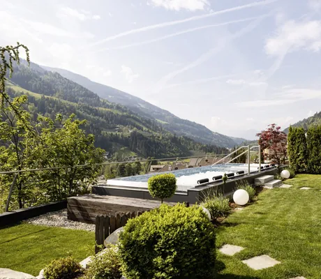 großer Panorama-Whirlpool des Alpenschlössel inmitten grüner Natur, umgeben von Bergen