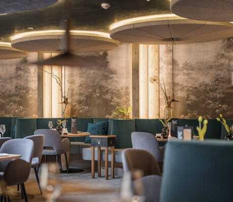 Blick in das modern eingerichtete Restaurant des Alpenschlössel mit grauen Polsterstühlen, grünen Sitzbänken und großen, runden Deckenlampen