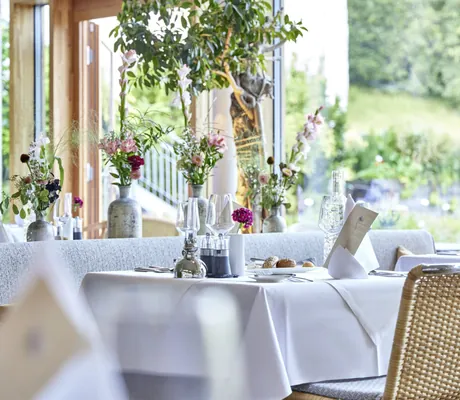 Restaurant im Das Kranzbach mit Korbstühlen und Steingut-Blumenvasen auf den eingedeckten Tischen