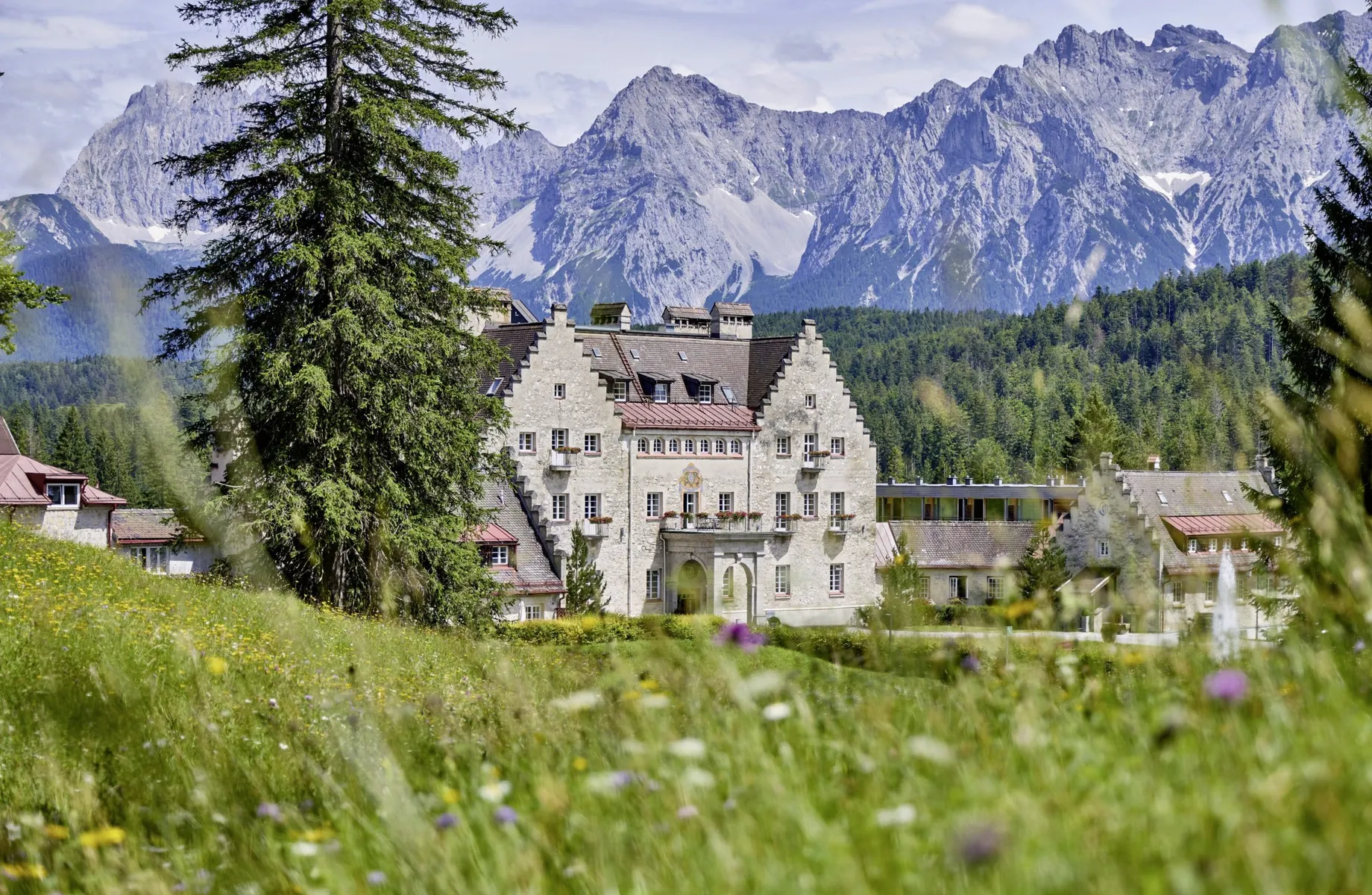 Englisches Schloss vom Das Kranzbach inmitten grüner Wiesen und Blick auf das Wettersteingebirge