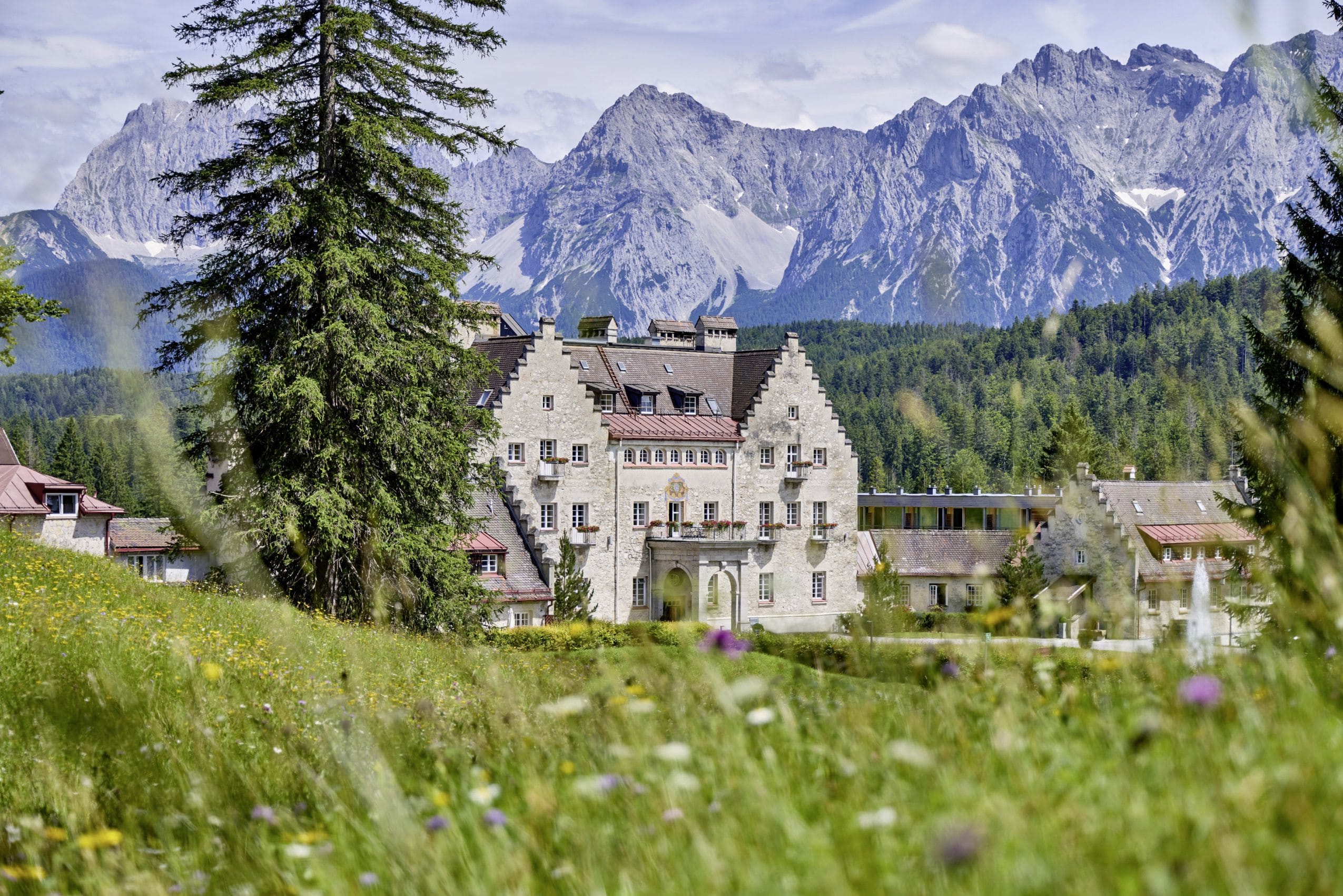 Englisches Schloss vom Das Kranzbach inmitten grüner Wiesen und Blick auf das Wettersteingebirge