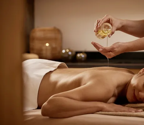 dunkelhaarige Frau erhält im Hanusel Hof eine Massage mit Öl aus einer Karaffe