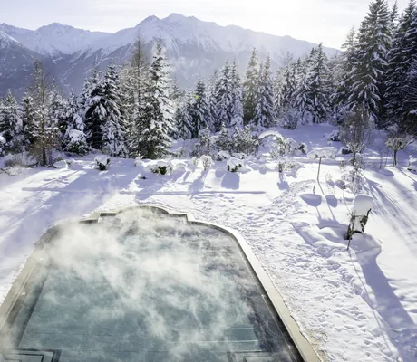 Outdoorpool des Interalpen-Hotel Tyrol in der tief verschneiten Gartenlandschaft mit Blick auf die Berge