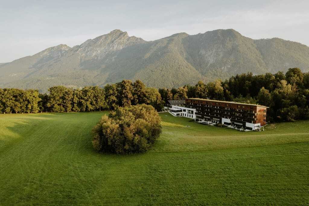 Gesamtansicht des Klosterhof - Alpine Hideaway & Spa inmitten grüner Wiesen und Bayerischen Bergen im Hintergrund