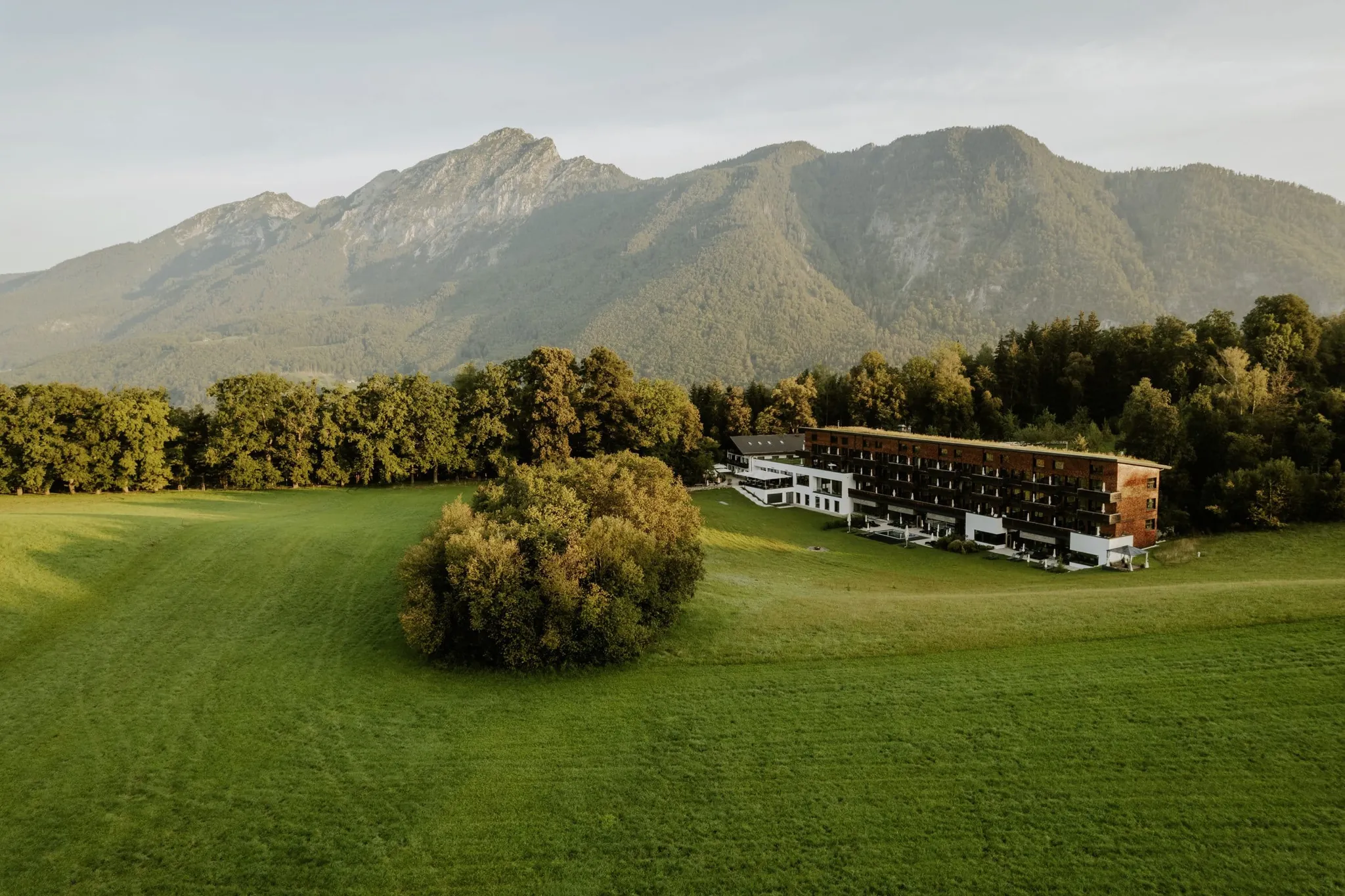 Gesamtansicht des Klosterhof - Alpine Hideaway & Spa inmitten grüner Wiesen und Bayerischen Bergen im Hintergrund