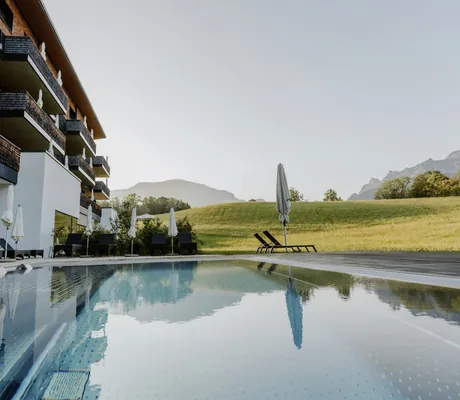 Outdoorpool des Klosterhof - Alpine Hideaway & Spa mit Blick auf die Wiese vor dem Hotel
