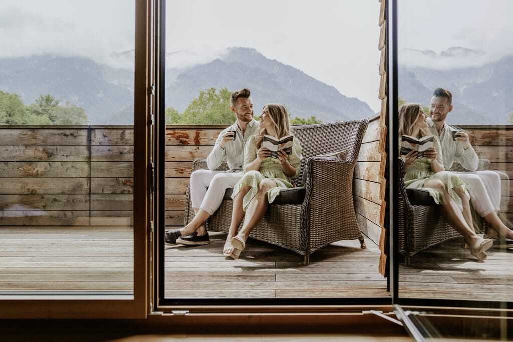 Paar sitzt im Korbsofa auf dem Balkon des Klosterhof - Alpine Hideaway & Spa und liest ein Buch