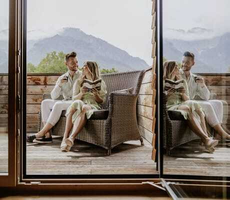 Paar sitzt im Korbsofa auf dem Balkon des Klosterhof - Alpine Hideaway & Spa und liest ein Buch