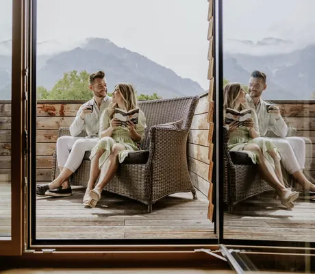 Paar sitzt im Korbsofa auf dem Balkon des Klosterhof - Alpine Hideaway & Spa und liest ein Buch