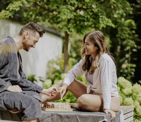 Mann in Bademantel udn Frau in Bluse sitzen auf Holzponton des Klosterhof - Alpine Hideaway & Spa und spielen Schach